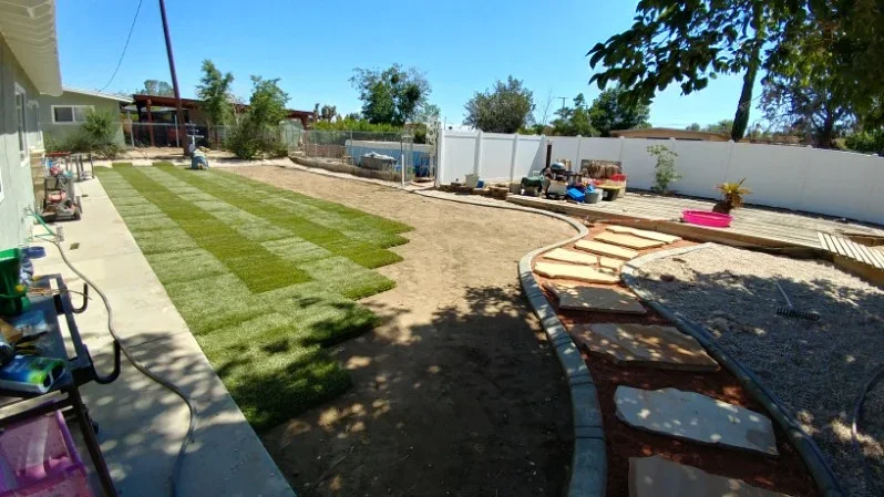 Newly sodded lawn with concrete borders, gravel pathways, and vinyl fencing in residential backyard