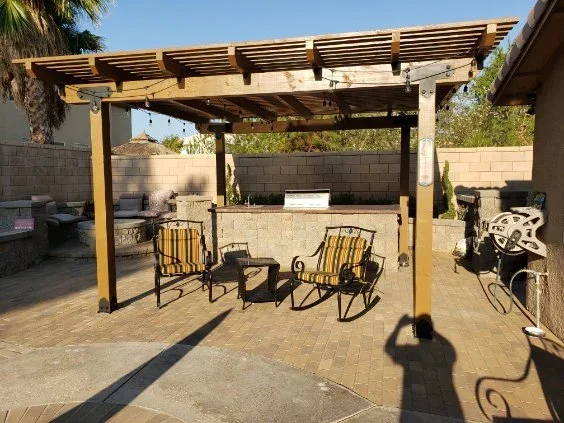 Wood pergola with slatted roof over paver patio, lounge seating, and concrete block outdoor kitchen counter