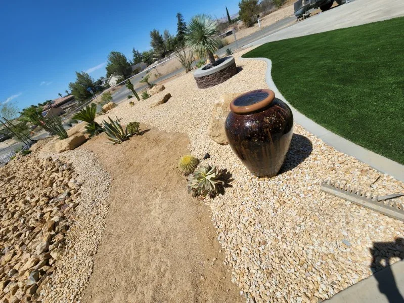 Synthetic turf, decorative gravel, ceramic water feature, and desert plants with concrete edging