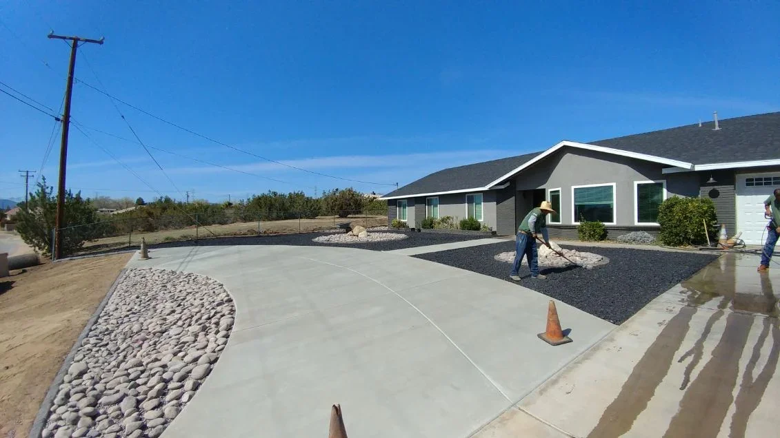 Concrete driveway with dark mulch beds, river rock borders, and landscape edging during installation