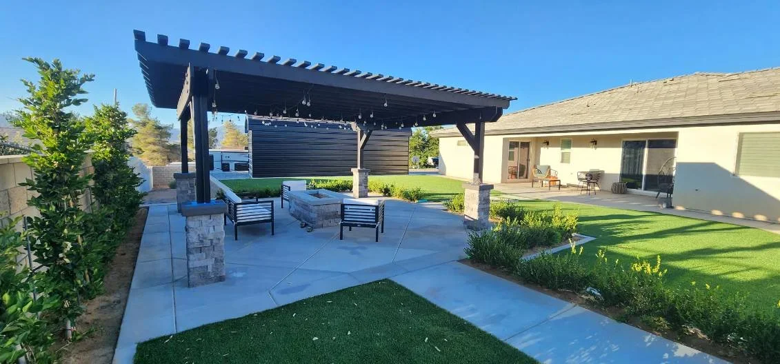Black pergola over concrete patio with stone planters and seating areas