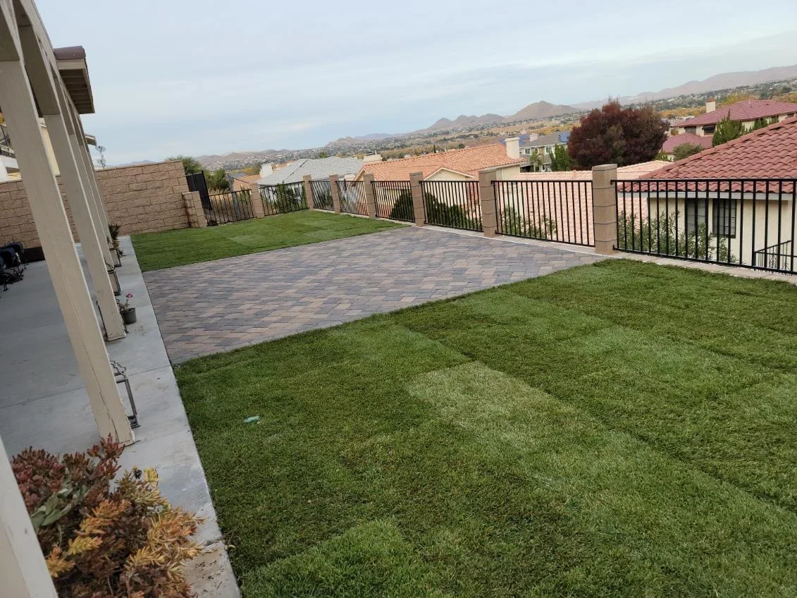 Paver patio with herringbone pattern, installed turf lawn, and wrought iron railings