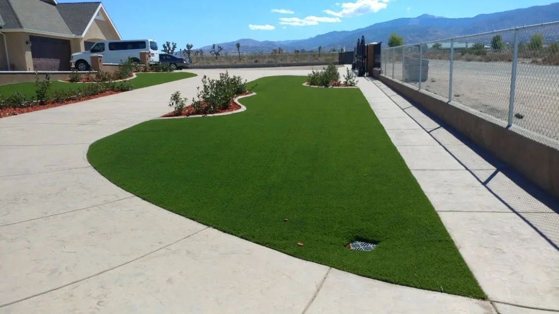 Synthetic turf lawn with curved planting beds, red mulch, concrete walkways, and metal fence edging
