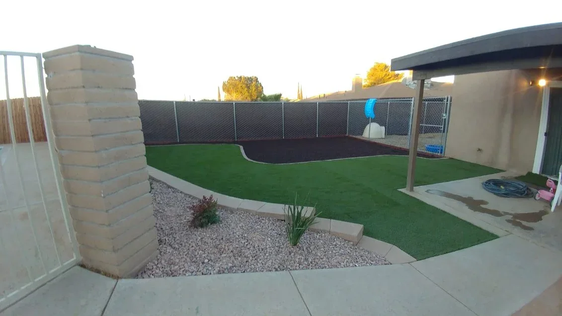 Synthetic turf yard with gravel beds, concrete patio, pergola, and chain-link fence