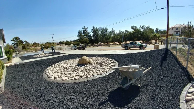 Dark gravel landscape with white river rock circular pattern, boulder, and concrete edging