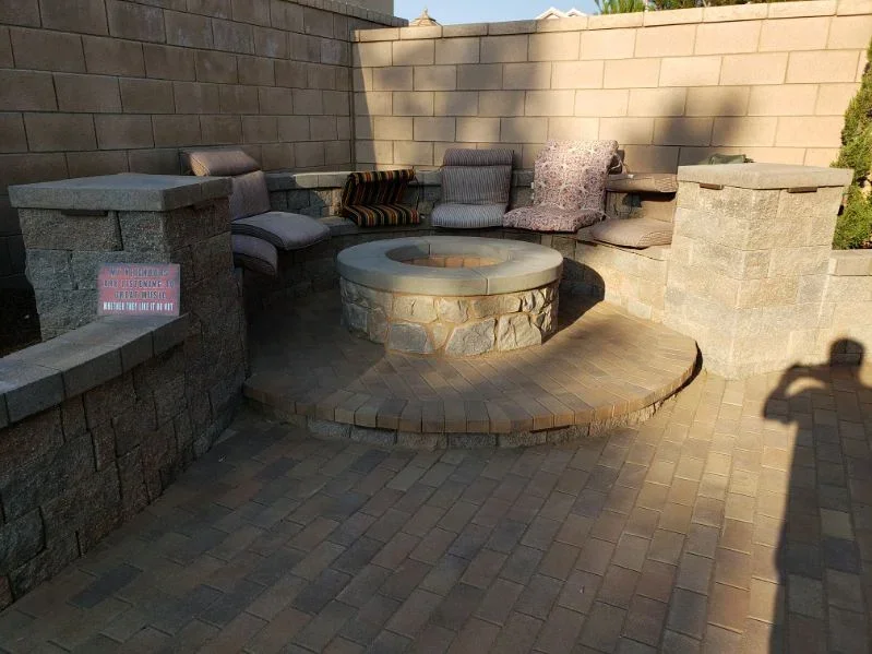 Circular stone fire pit with paver patio and concrete seating walls in backyard setting