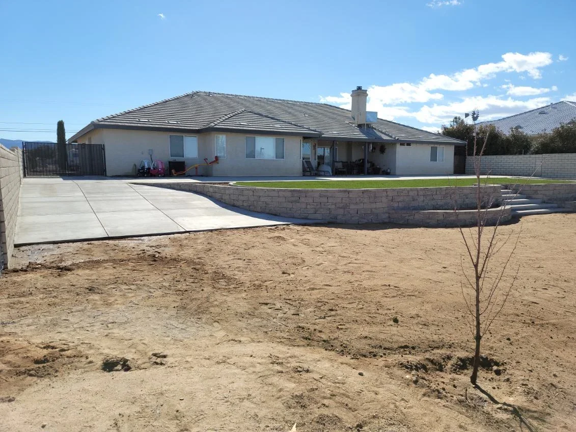 Concrete patio with curved stone retaining wall and new lawn installation