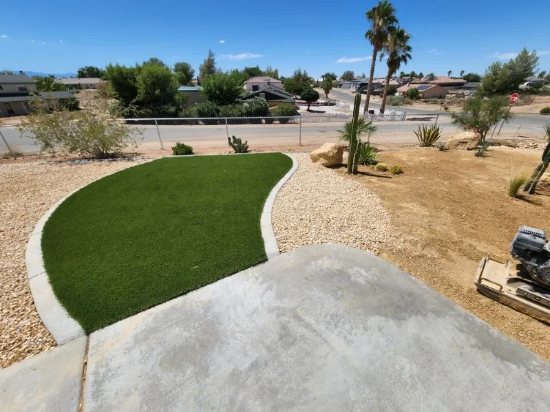 Curved synthetic turf lawn with white concrete edging, decomposed granite, and desert plants in residential yard