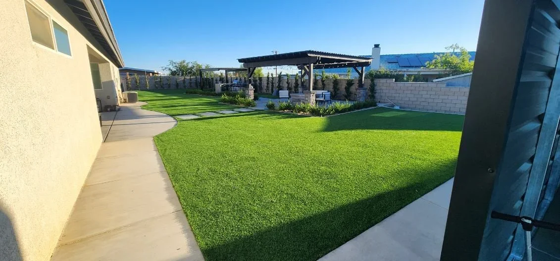 Synthetic turf lawn with concrete patio, raised planters, black pergola, and composite fencing