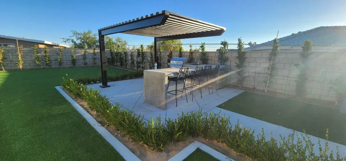 Concrete patio with black pergola, concrete island bar, synthetic turf, and planted landscape beds