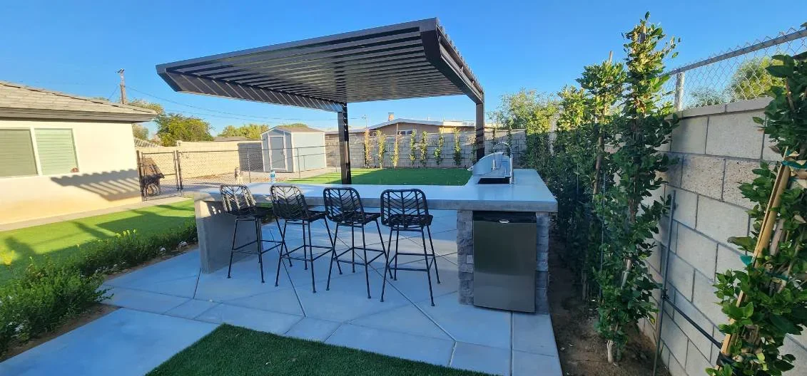 Concrete patio with outdoor kitchen, black pergola, bar seating, and grill installation