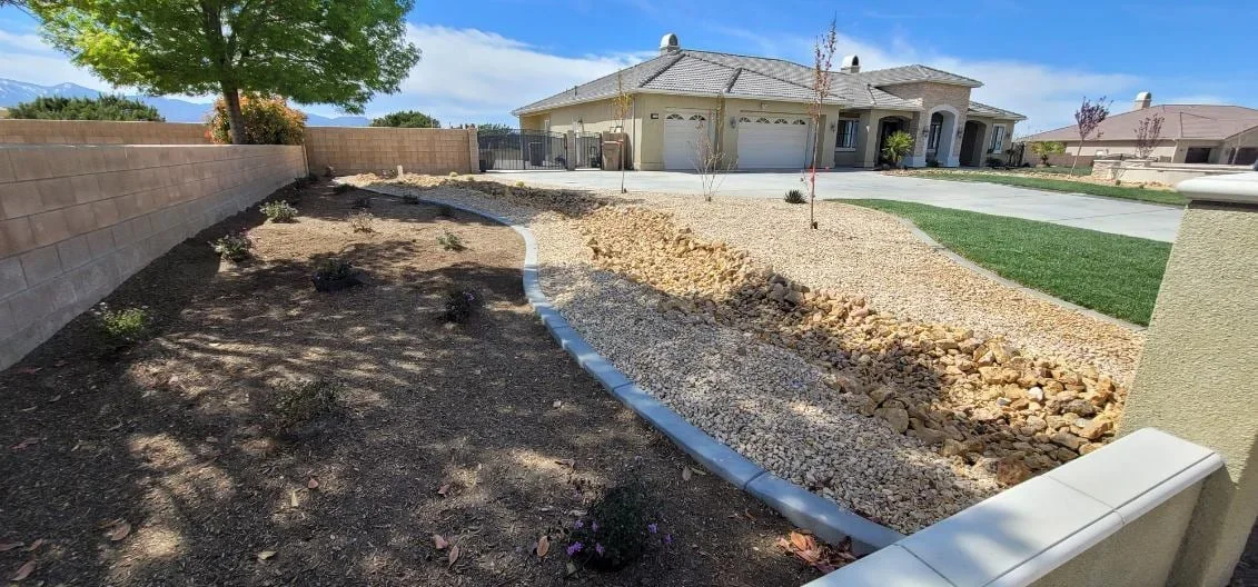 Landscape grading with drainage edging, gravel base, and newly planted trees in residential yard