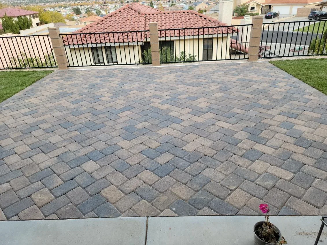Herringbone paver patio with gray and tan pavers, metal railing, and lawn borders