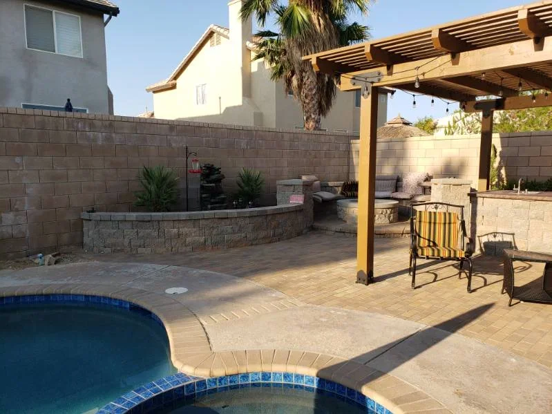 Paver patio with wooden pergola, stone fire pit, and concrete block retaining walls